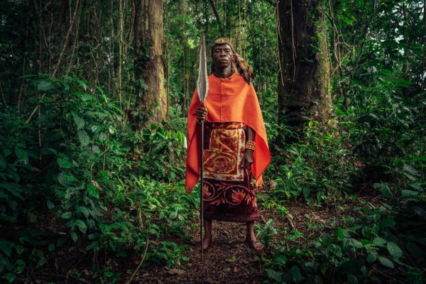 Chief Wilondo Baswa, gewoontehoofd van de Ntombezale-stam, Lobalu-clan, van Mai Ndombe, DRC. Het gewoontehoofd is de vertegenwoordiger van de voorouders in zijn gemeenschap. Deze kleding weerspiegelt de voorouderlijke macht en wordt vaak gedragen tijdens grote traditionele ceremonies. De adelaarsveren en de luipaardenhuid staan voor voorouderlijke kracht, terwijl de rode kleur staat voor macht. De voorouderlijke speer of machete vertegenwoordigt een krijger. Fotocredit: Filip C. Agoo voor Wildlife Works Carbon.